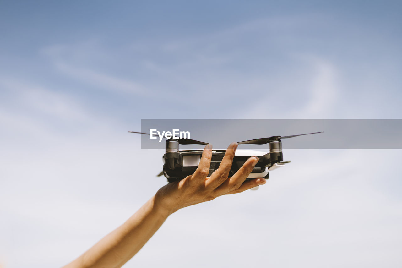 Hand of mature woman holding drone against sky during sunny day