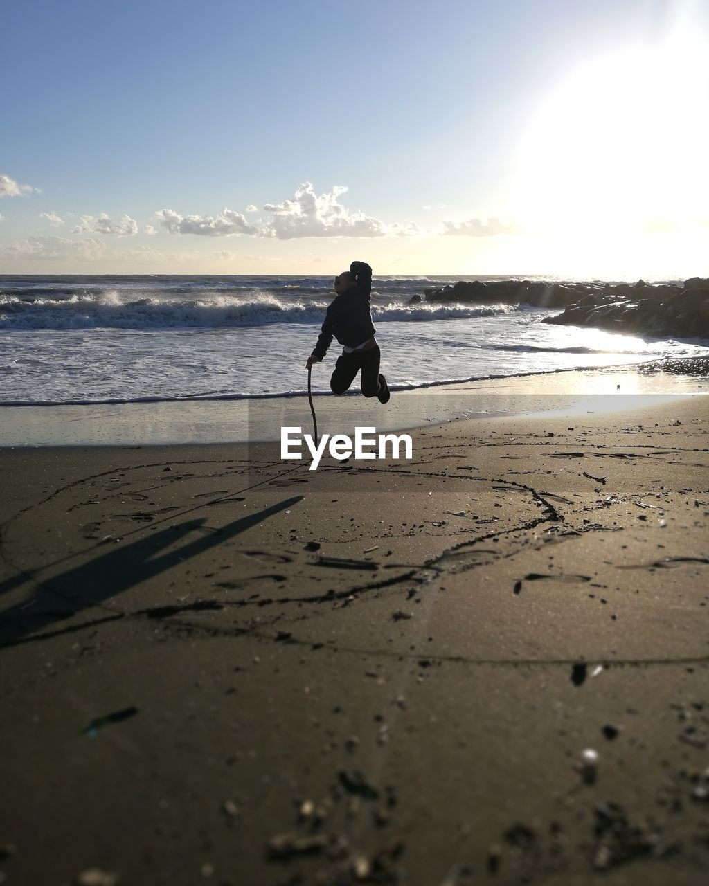 Silhouette girl jumping in mid-air at beach against sky during sunset