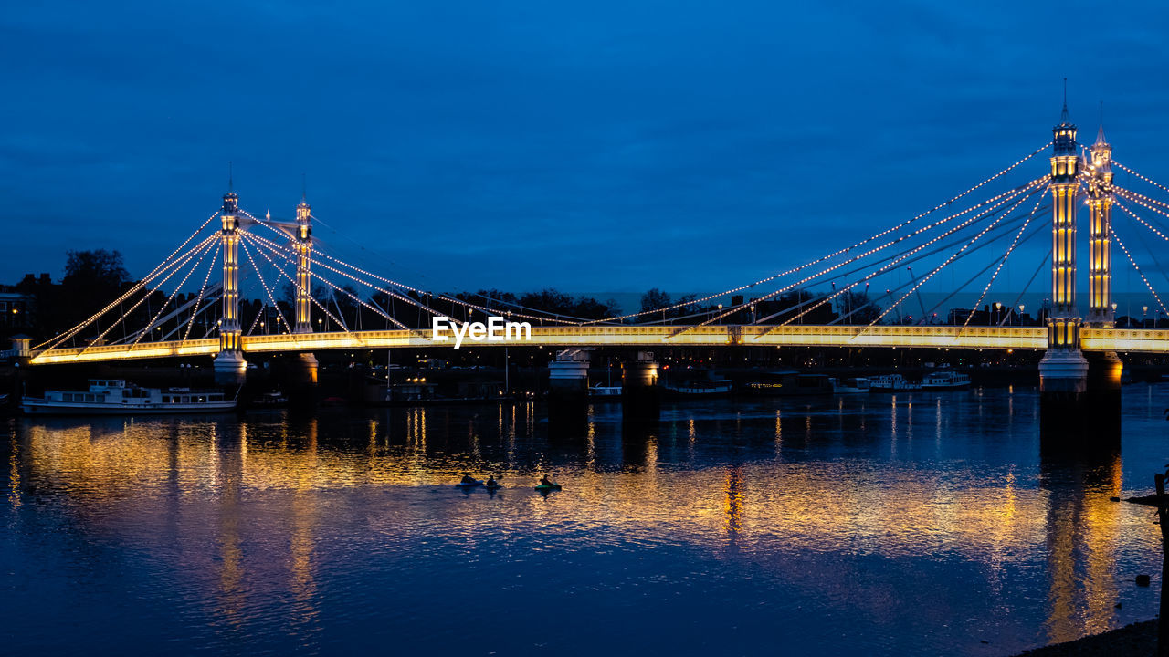 Illuminated bridge over calm river against blue sky