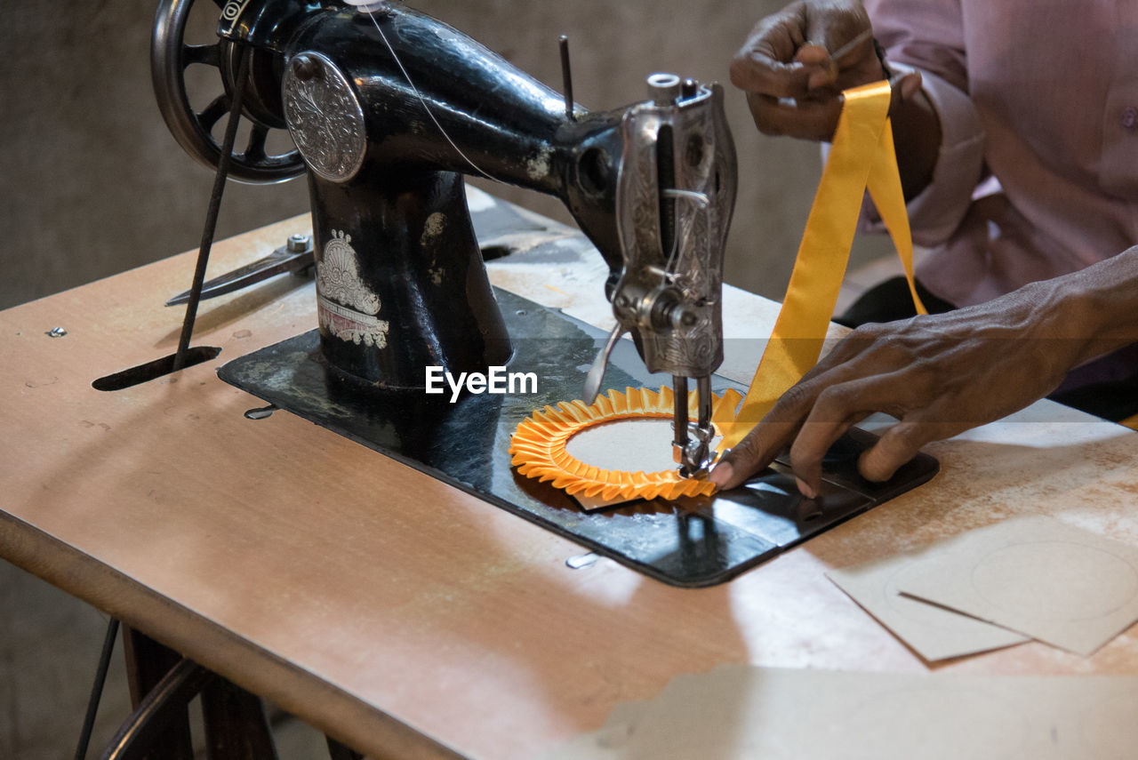 Midsection of tailor using sewing machine while stitching textile