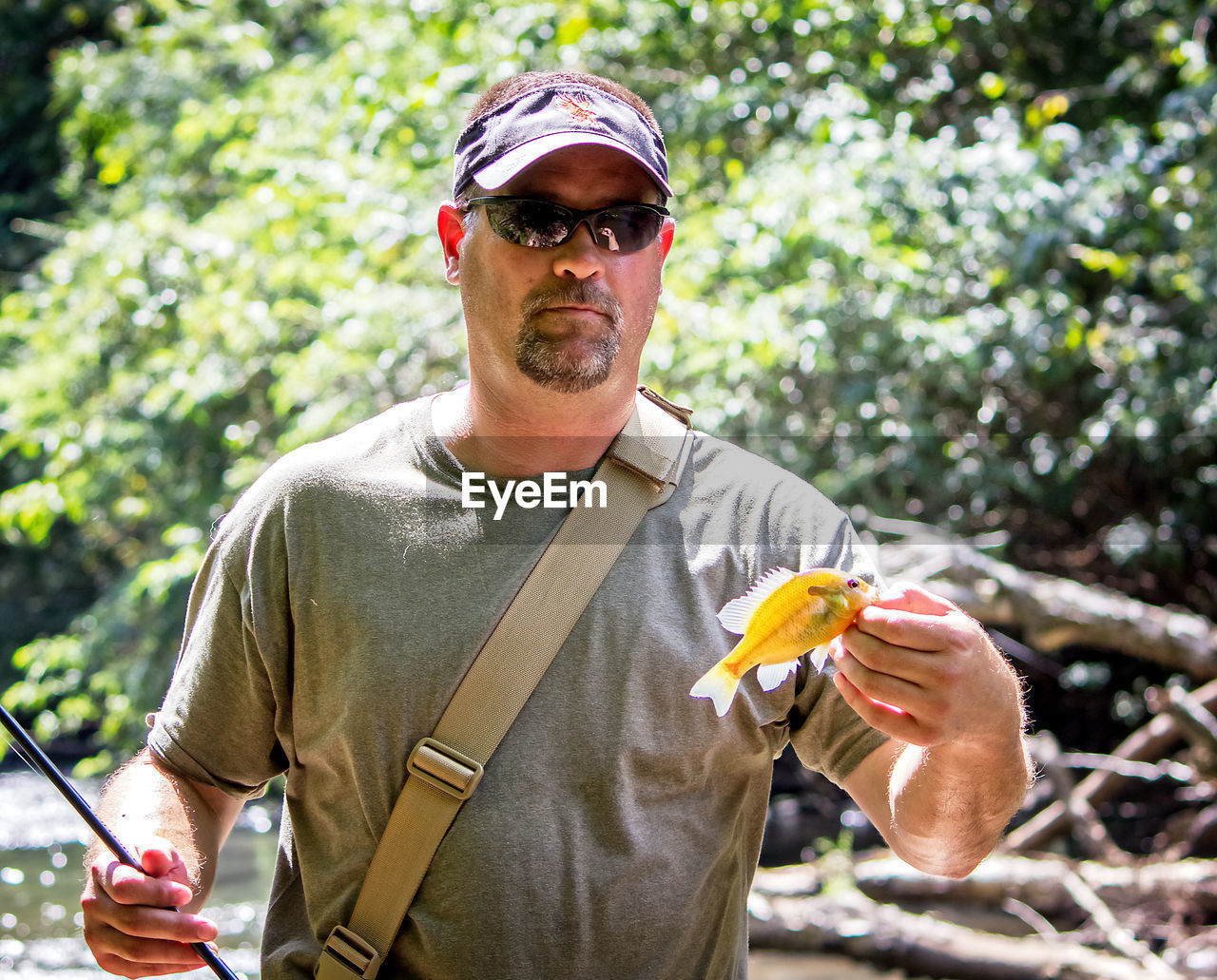 Portrait of man holding fish while fishing in lake