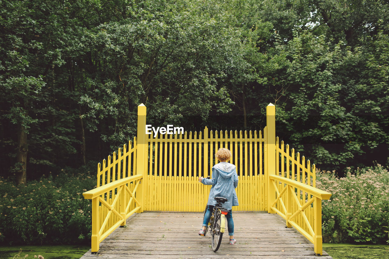Rear view of woman riding bicycle on footbridge against trees