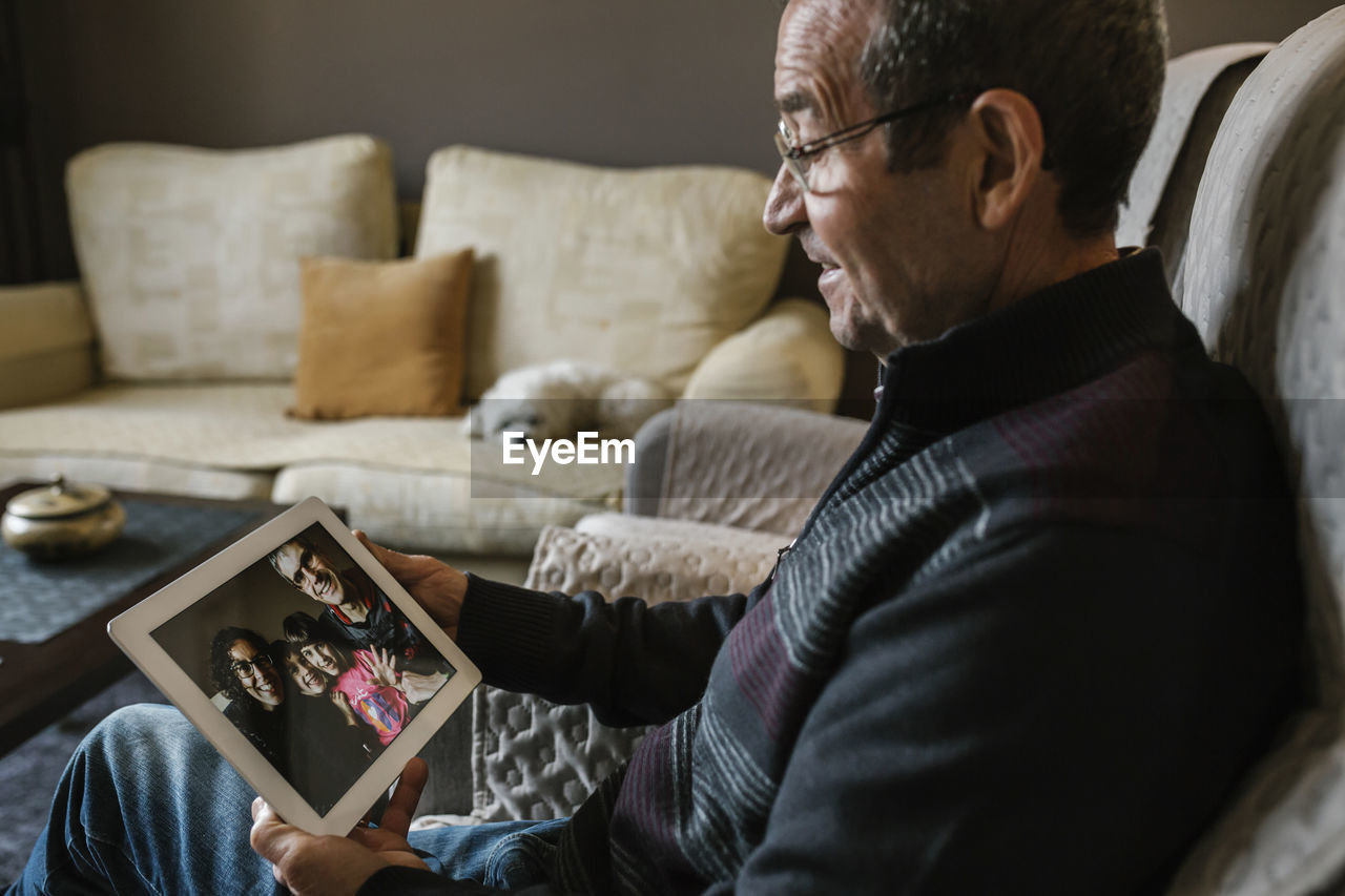 Smiling senior man on video call with his grandchildren through digital tablet at home during covid-19