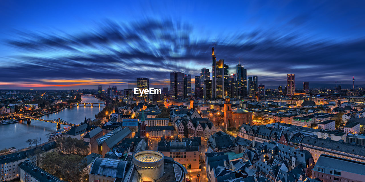 High angle view of buildings in illuminated city against cloudy sky at night