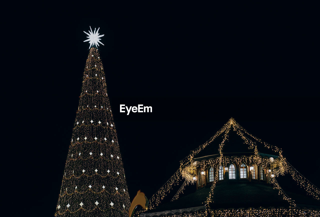 Low angle view of illuminated christmas tree against building at night