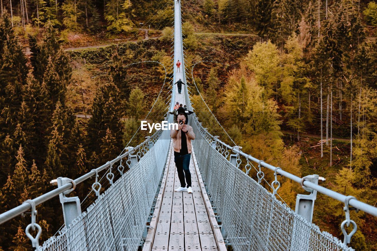 Man using smart phone while standing on footbridge in forest