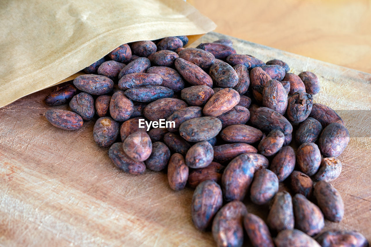 Roasted cocoa beans spilled out of the packaging on a wooden background.