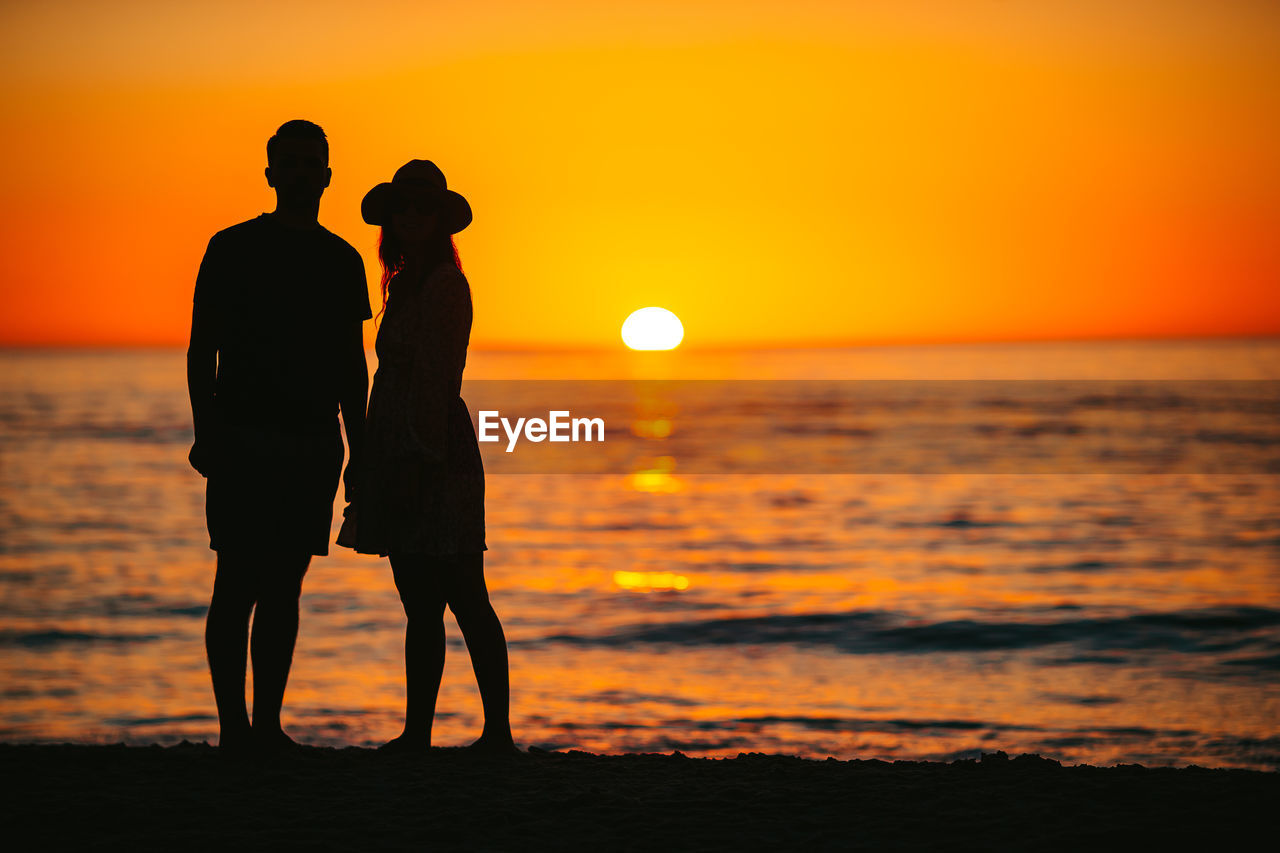 silhouette woman standing at beach against sky during sunset