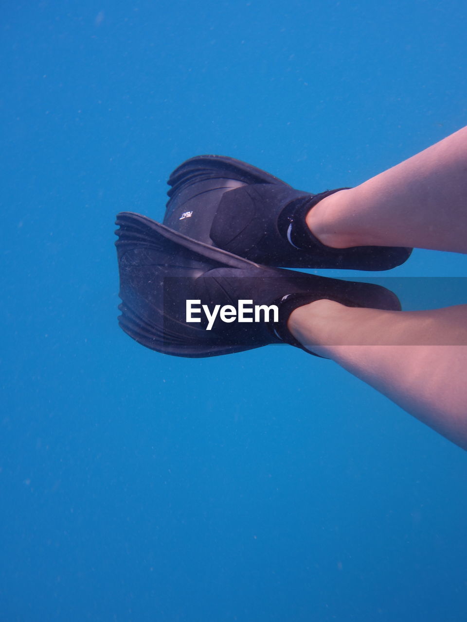 Low section of person wearing diving flipper while swimming in sea