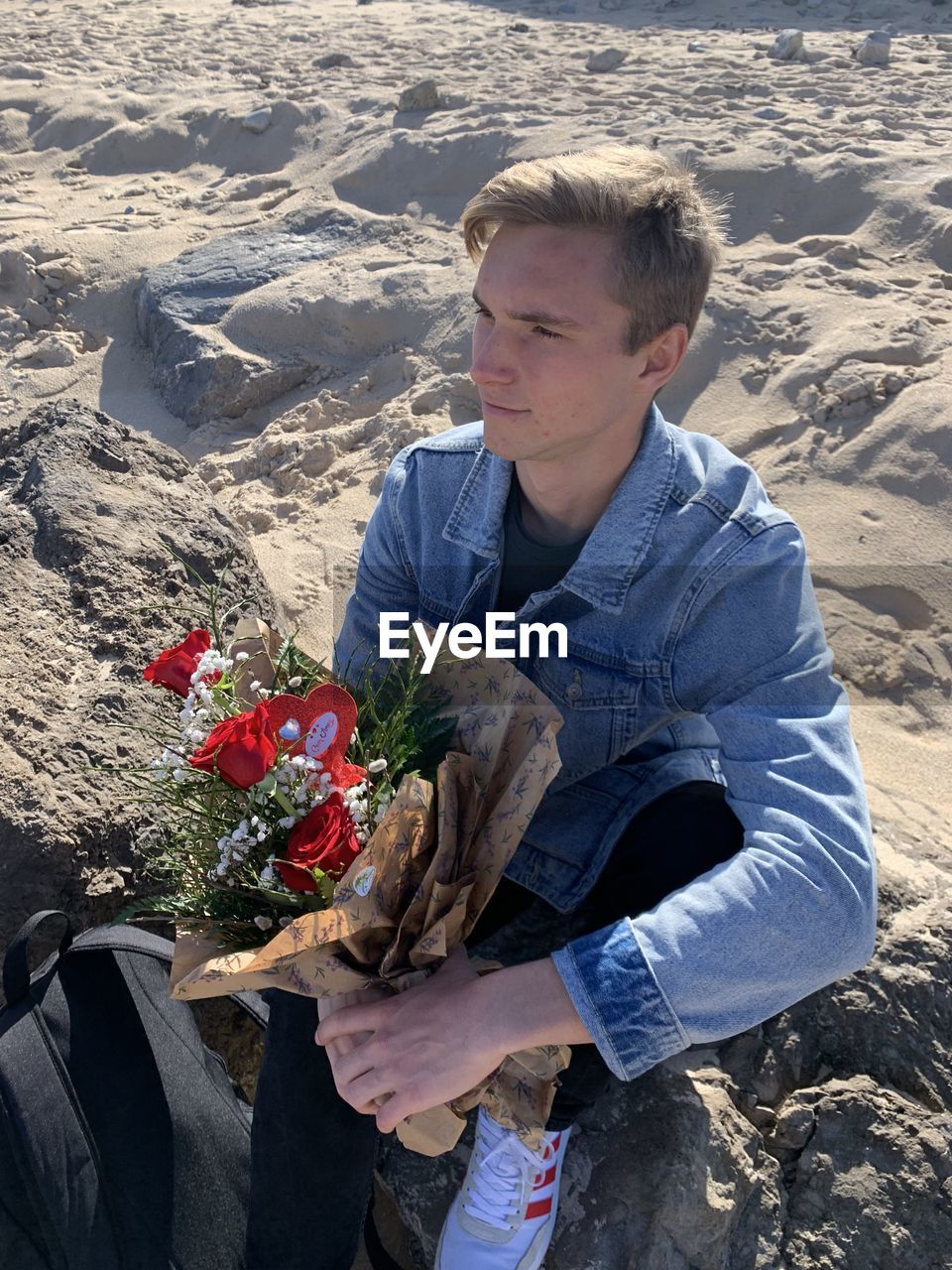 High angle view of man sitting on rock holding flowers