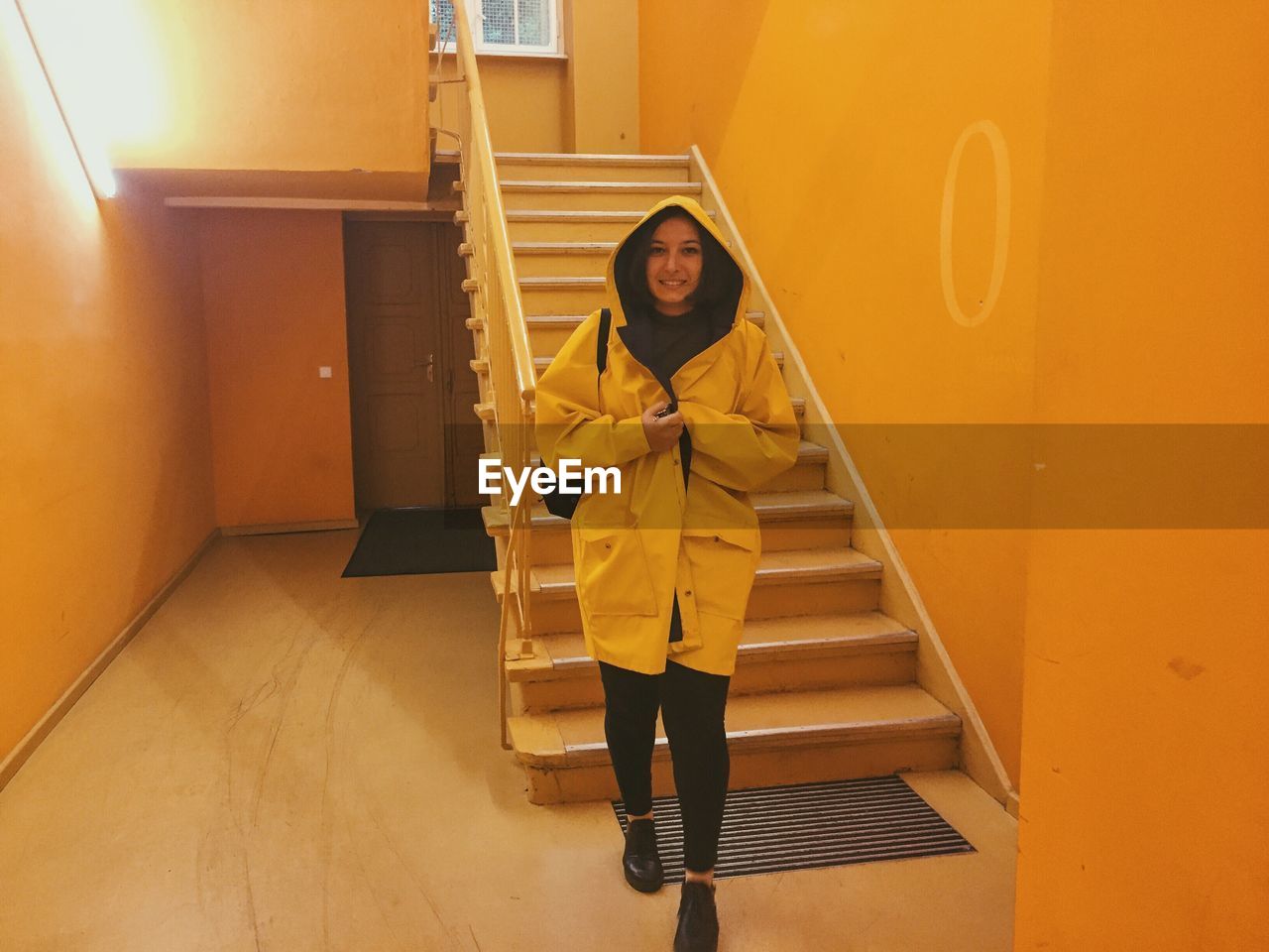 Full length portrait of woman wearing yellow raincoat by steps at home