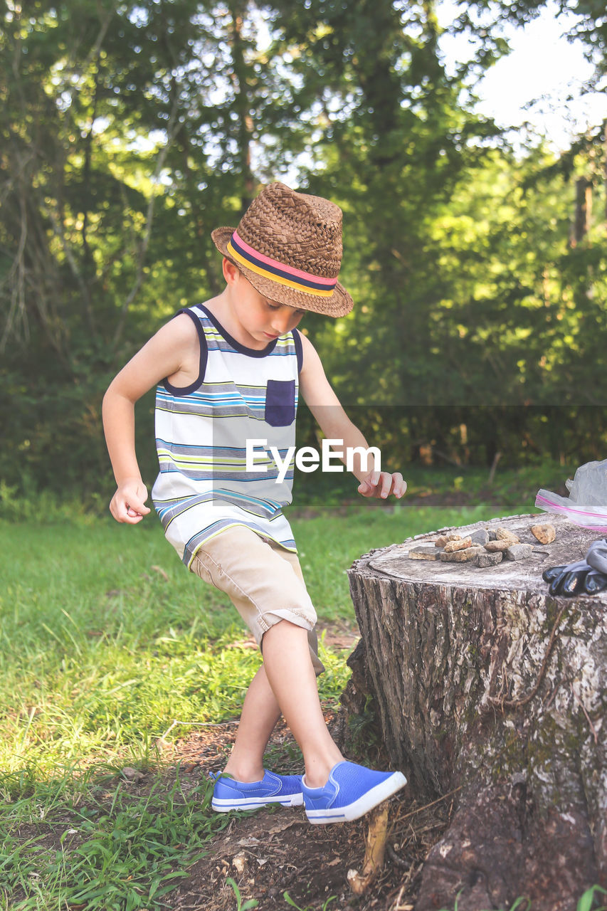 Boy wearing hat while standing by tree stump