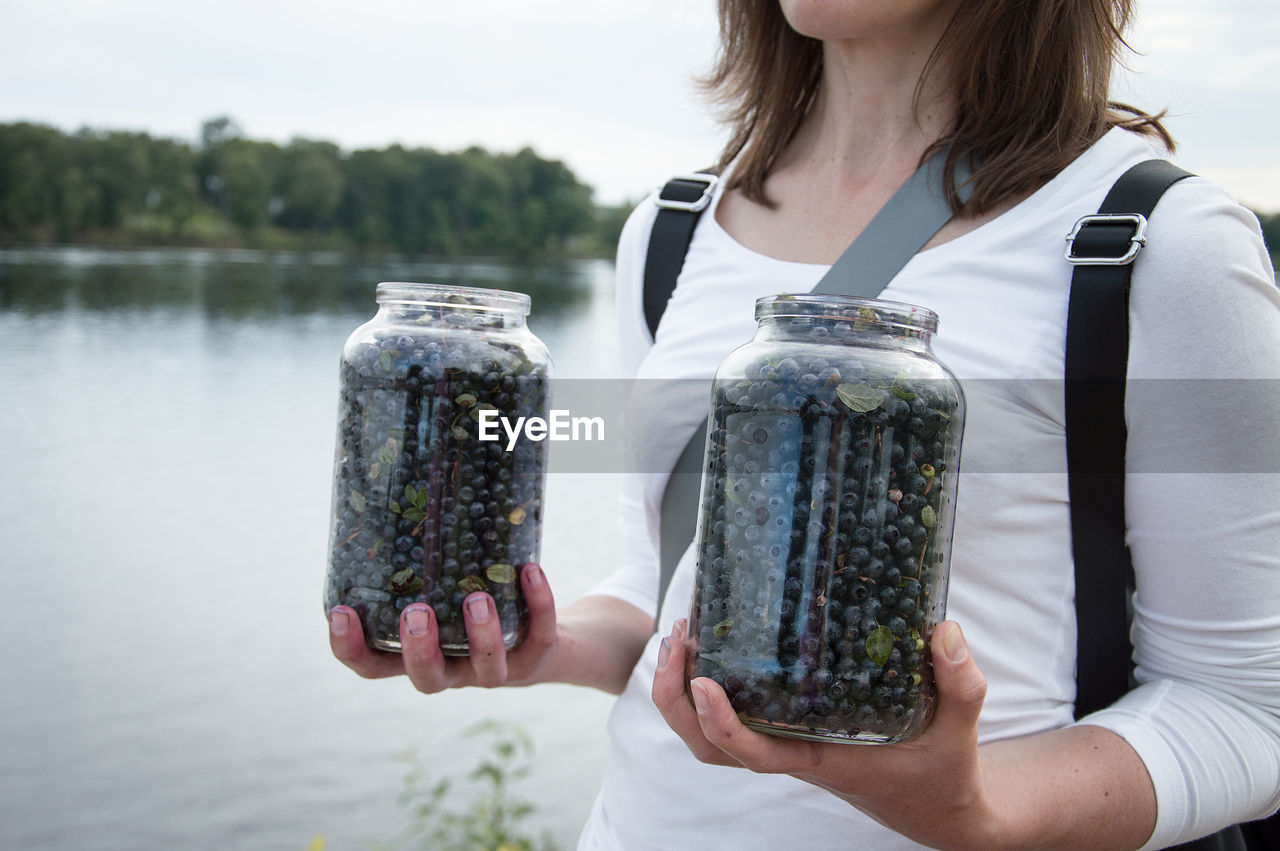 Midsection of woman holding blueberries in jars at lakeshore