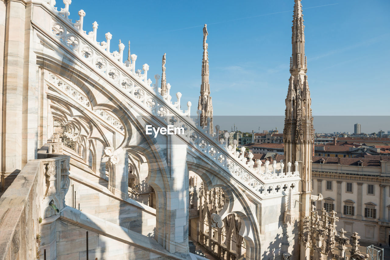 White statue on top of duomo cathedral and view to city of milan