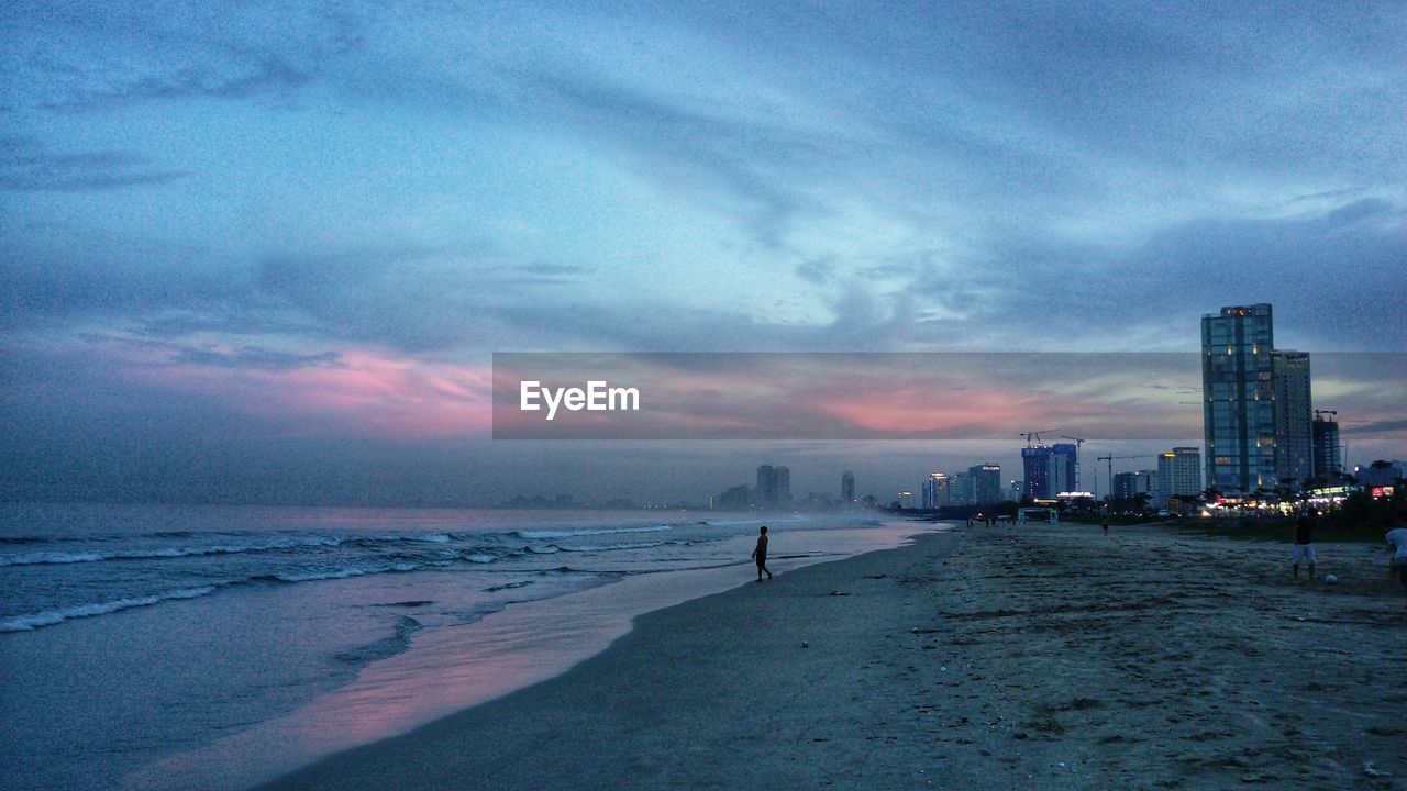 Scenic view of beach and buildings against sky at sunset