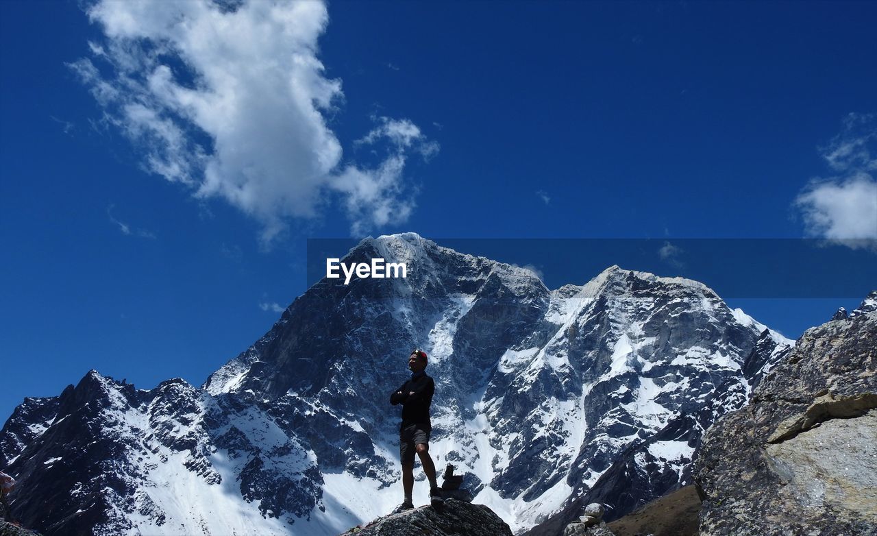 Man standing on snowcapped mountain against blue sky