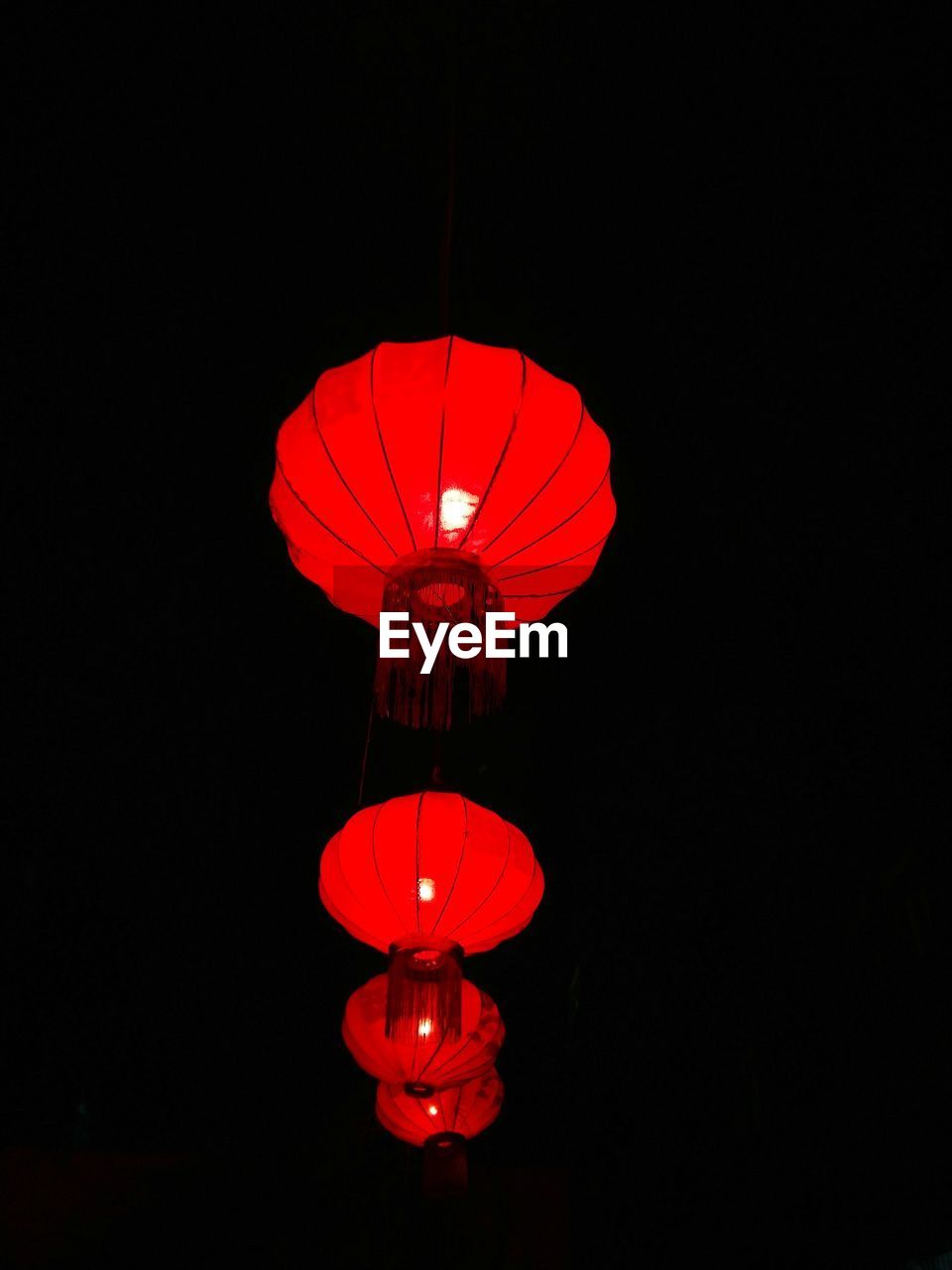 LOW ANGLE VIEW OF ILLUMINATED LANTERNS HANGING OVER BLACK BACKGROUND