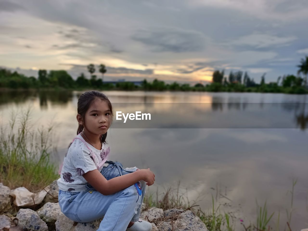 Portrait of girl sitting on lake against sky