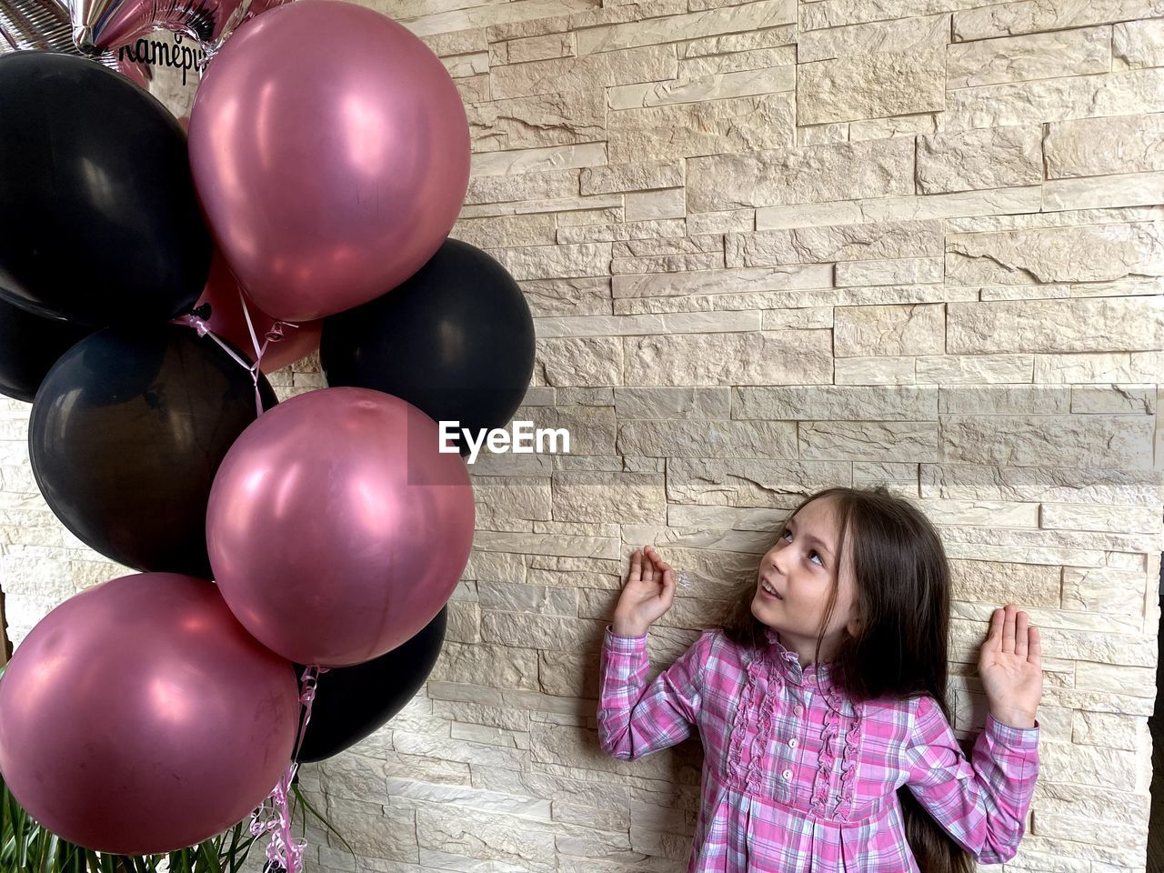 Cute girl standing by wall looking at balloon