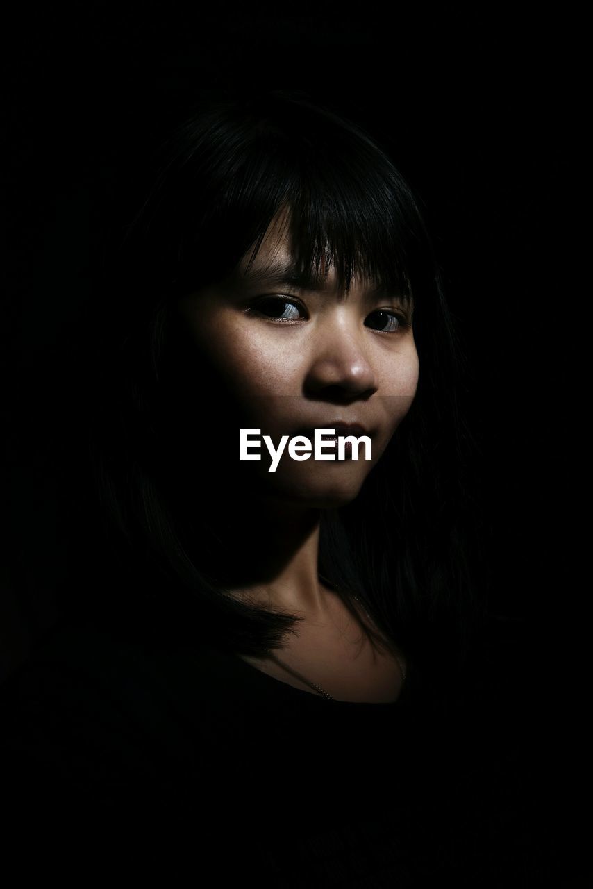 Close-up of a young woman over black background