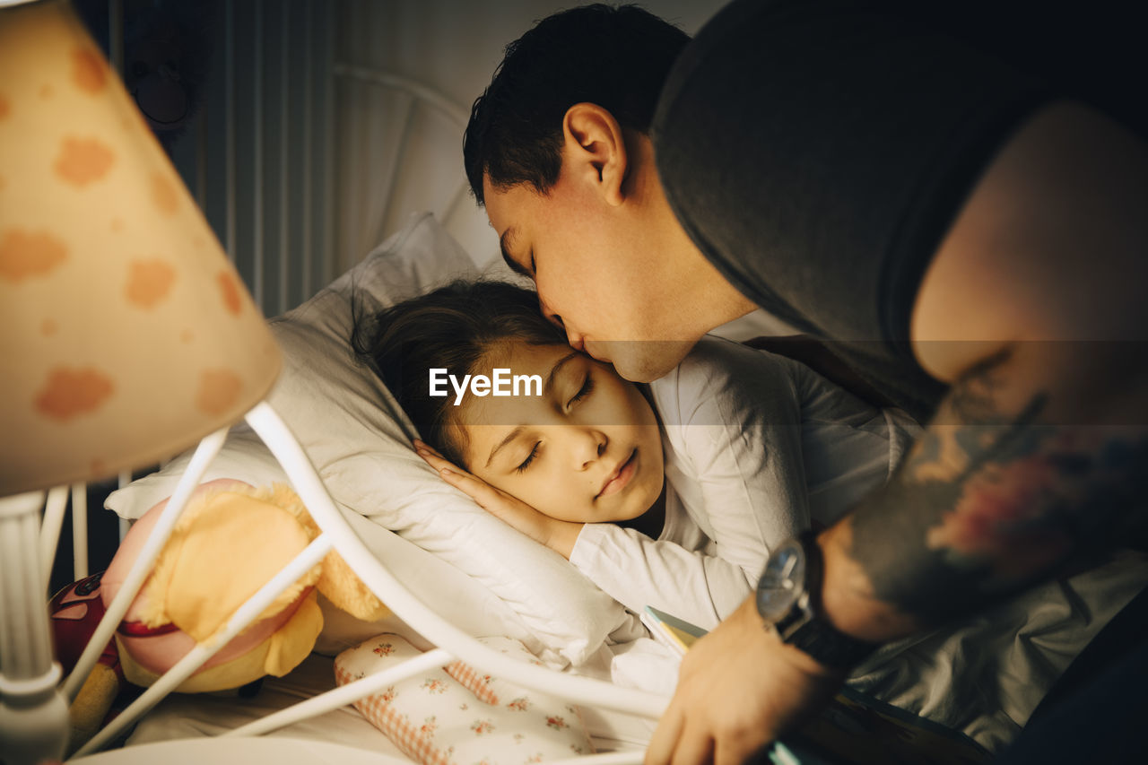 Father kissing daughter while sleeping in bed at home