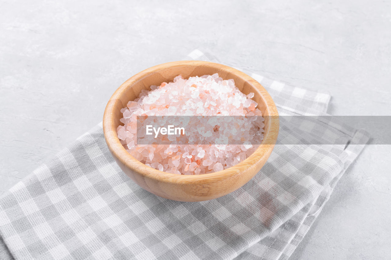 Pink himalayan salt in a wooden bowl on a light grey background, copy space