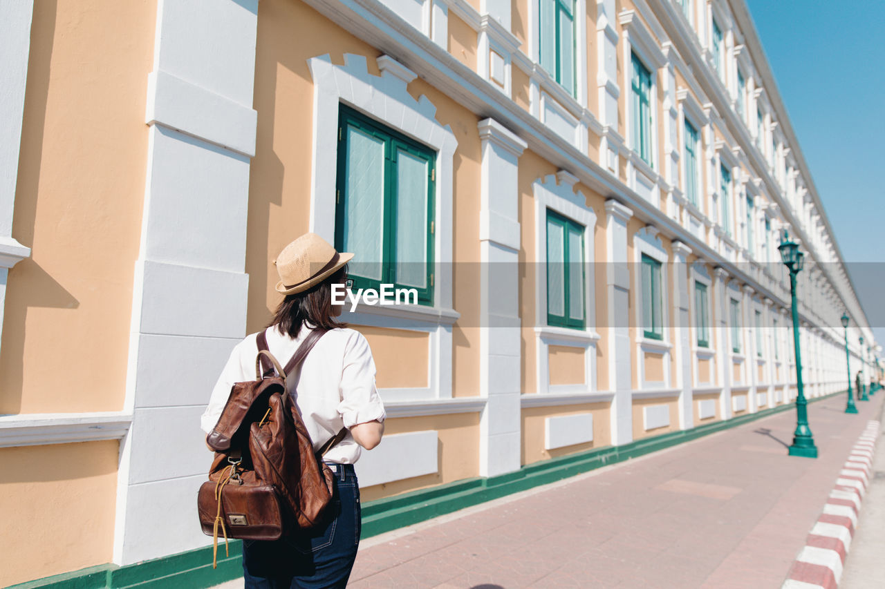 Behind of young asian woman with backpack and straw hat travel in old town bangkok, thailand