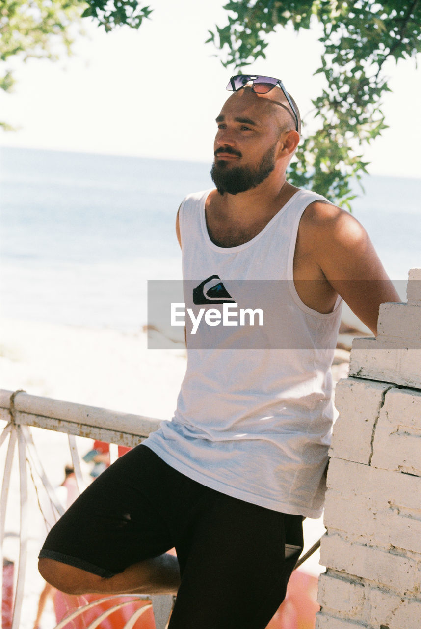 Thoughtful man looking away while standing against sea