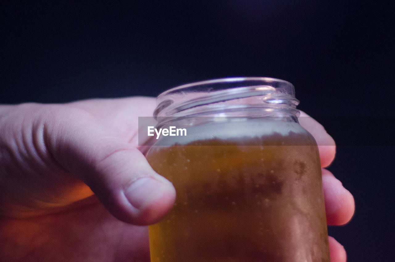 Cropped hand having beer in jar against black background