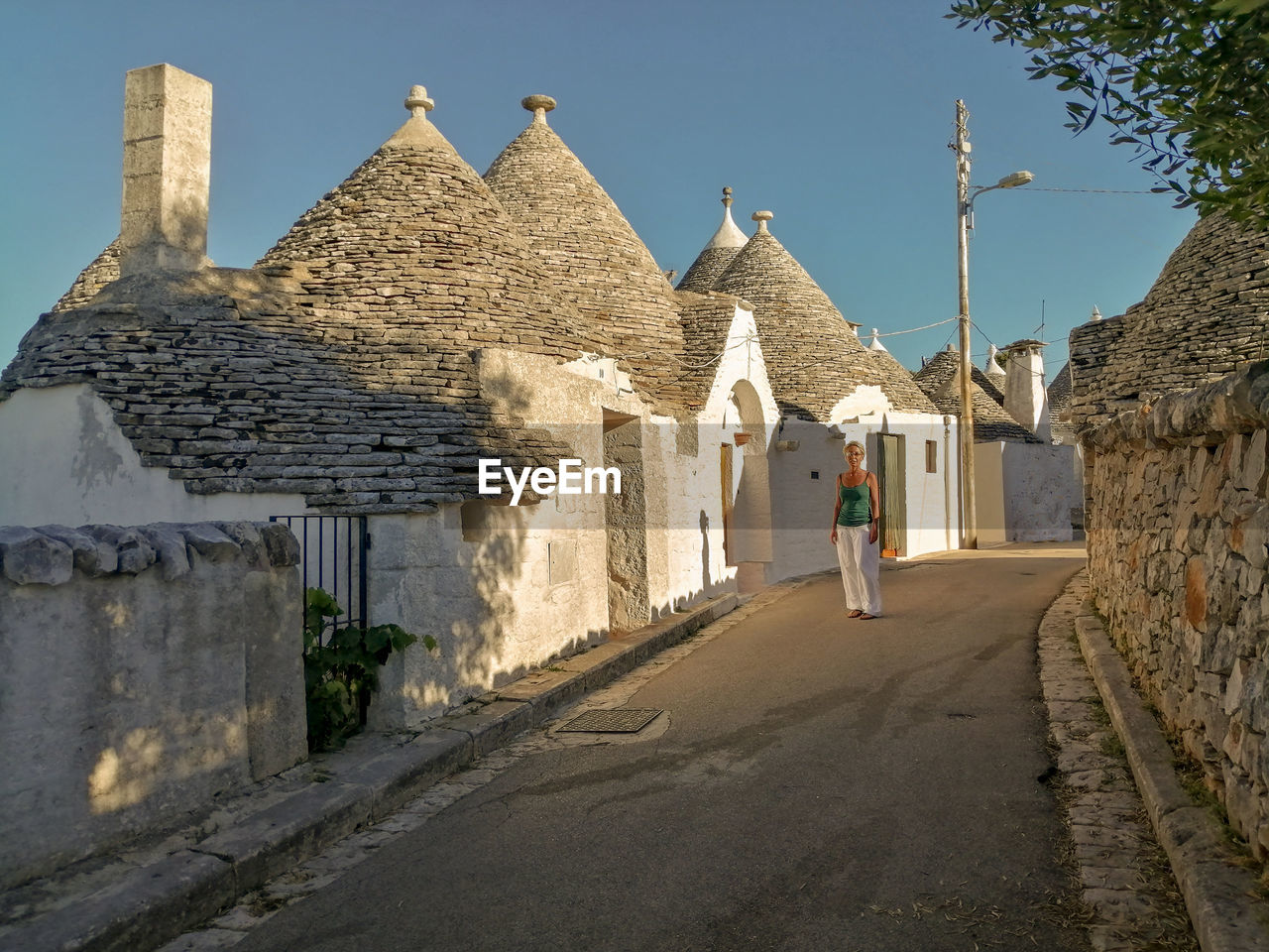 Rear view of woman walking by building against sky, in alberobello, apulia, italy 