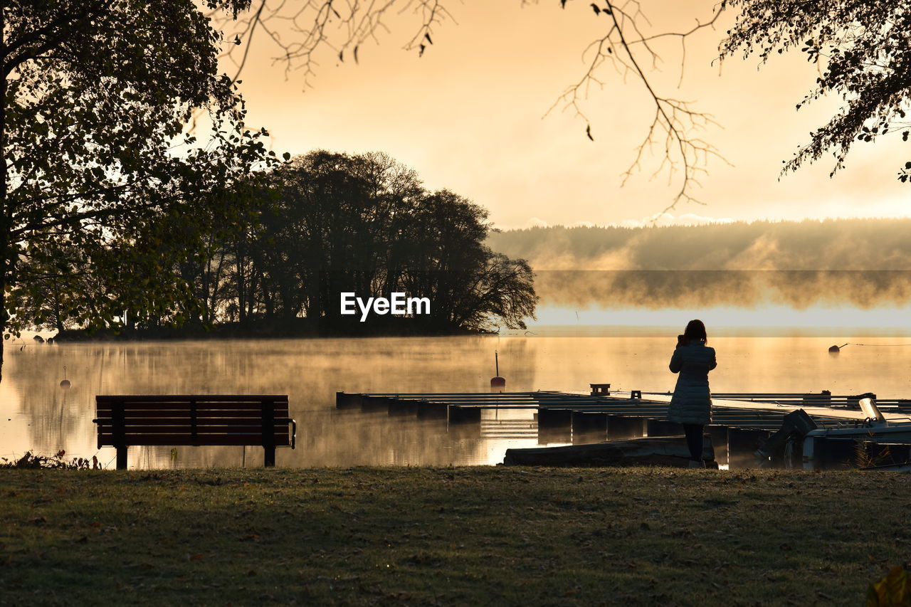 MAN SITTING ON BENCH BY LAKE AGAINST SKY