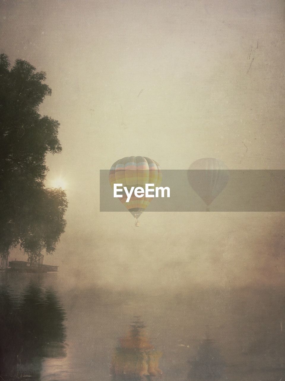 Reflection of hot air balloons and tree in calm lake