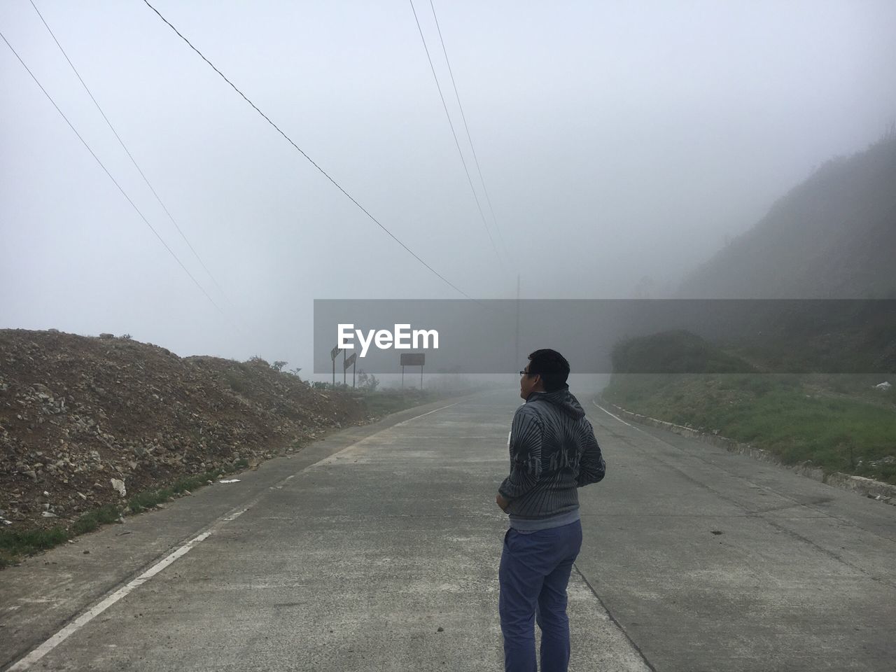 Rear view of young man standing on road during foggy weather