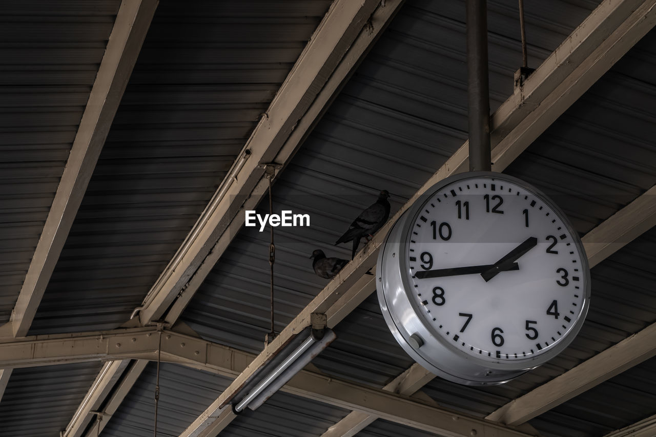 LOW ANGLE VIEW OF CLOCK HANGING ON CEILING OF BUILDING