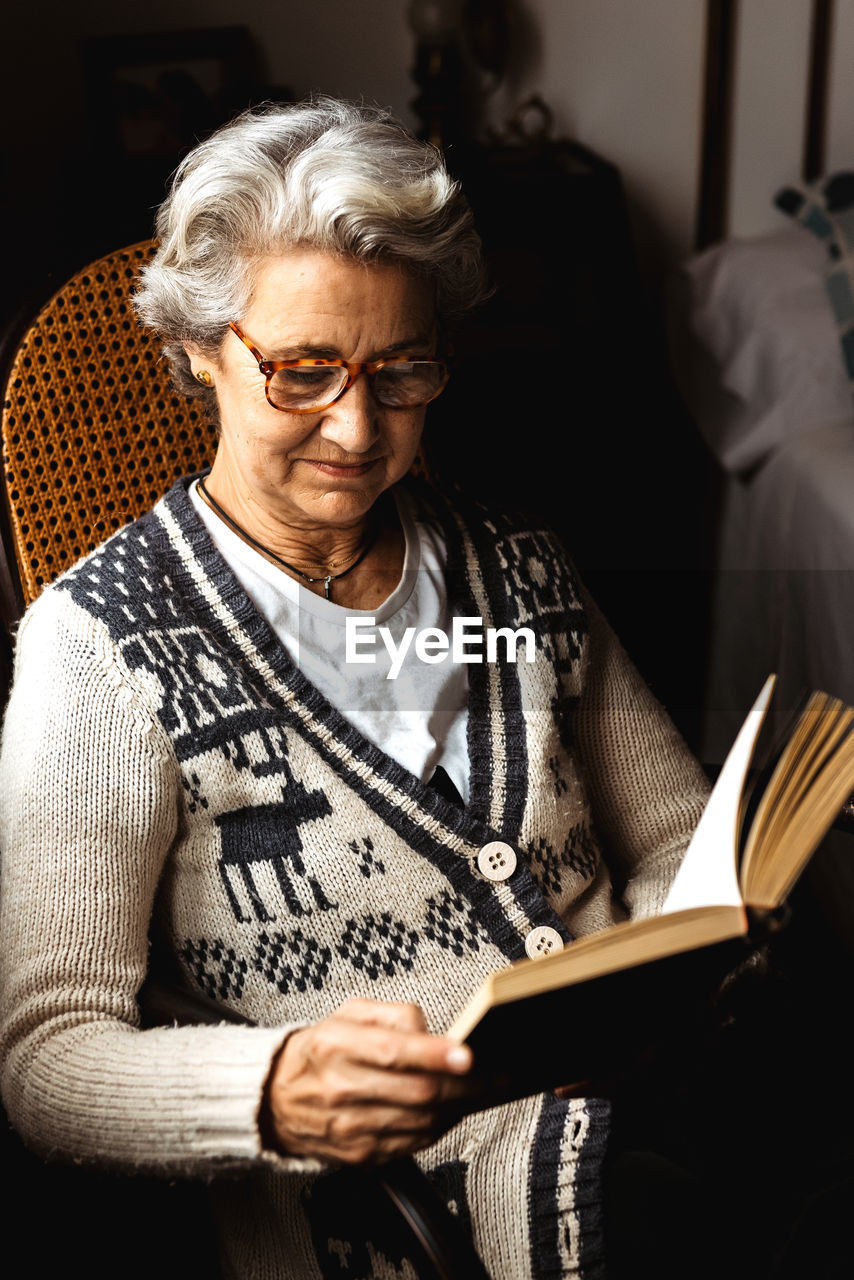 Elderly woman reading by window with enthusiasm