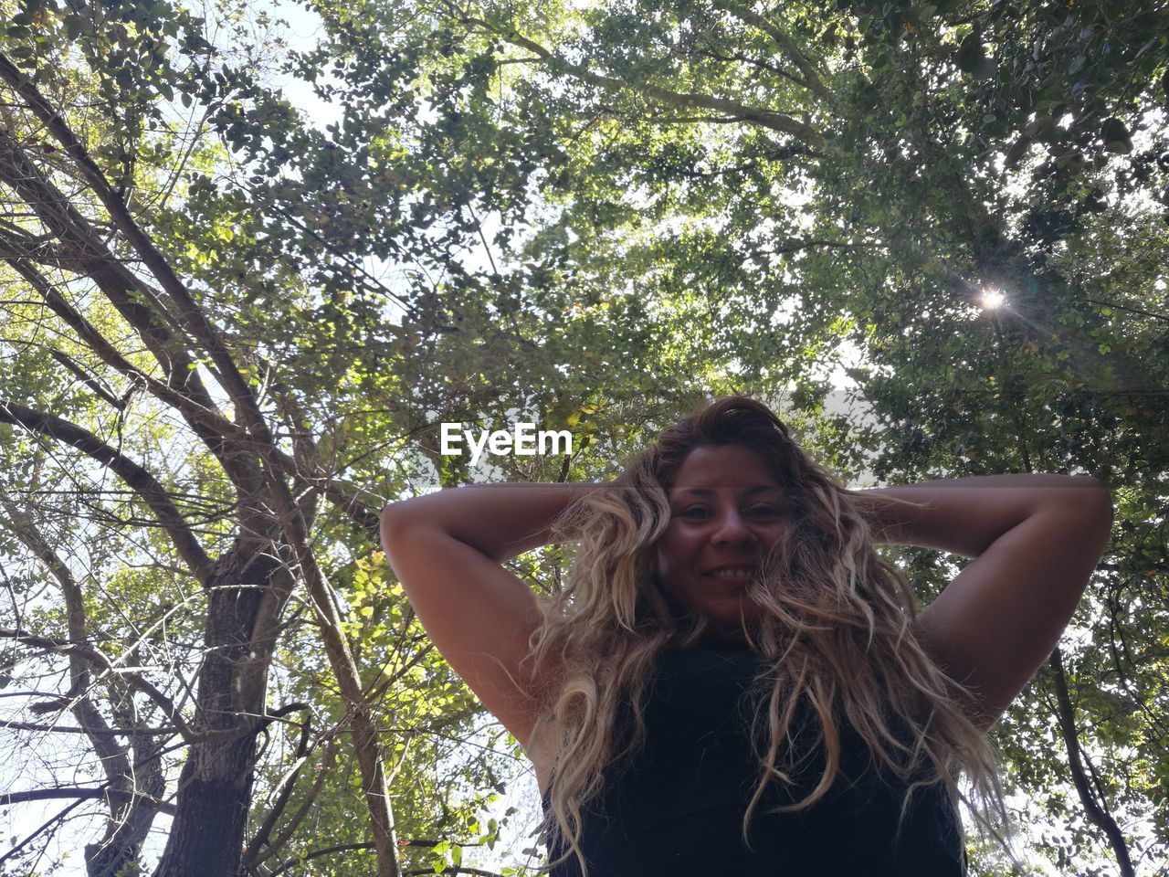 Low angle portrait of young woman standing against trees in forest