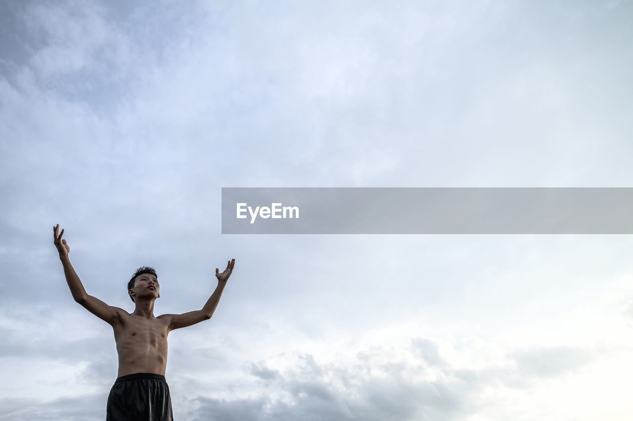 LOW ANGLE VIEW OF SHIRTLESS MAN AGAINST SKY