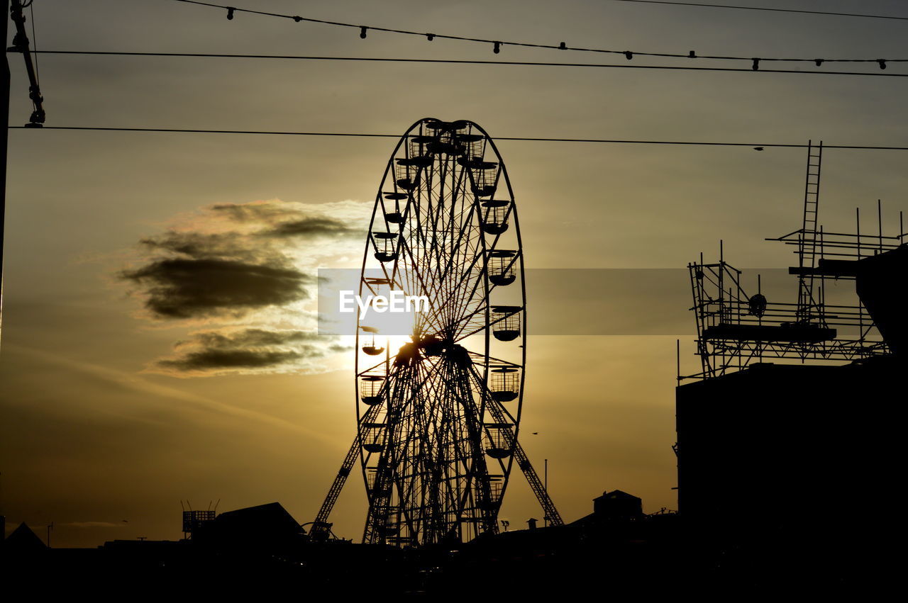 Ferris wheel on silhouette landscape against sunset