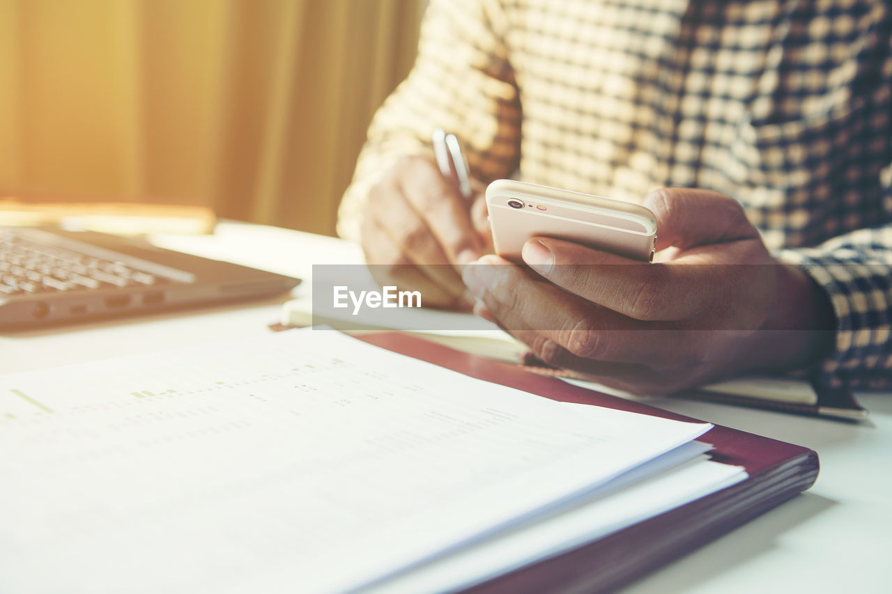 MIDSECTION OF MAN USING PHONE ON TABLE