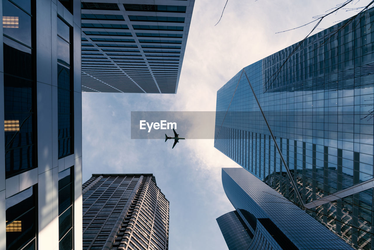 Low angle view of airplane flying over skyscrapers against sky