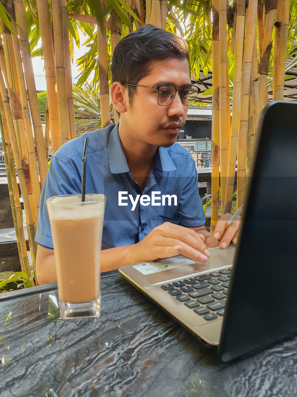 YOUNG MAN USING MOBILE PHONE WHILE SITTING IN TABLE