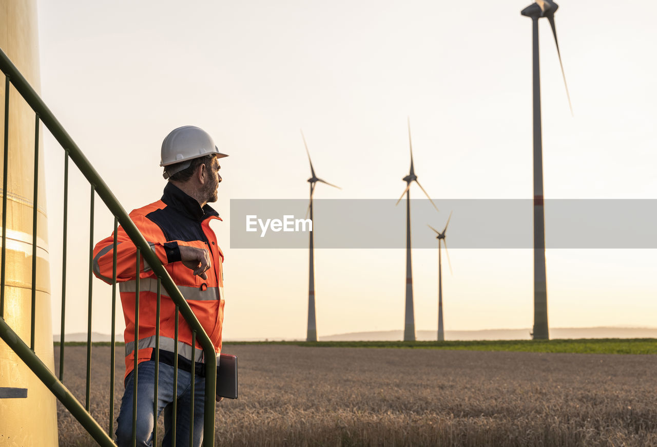 Male inspector at wind turbines during sunset