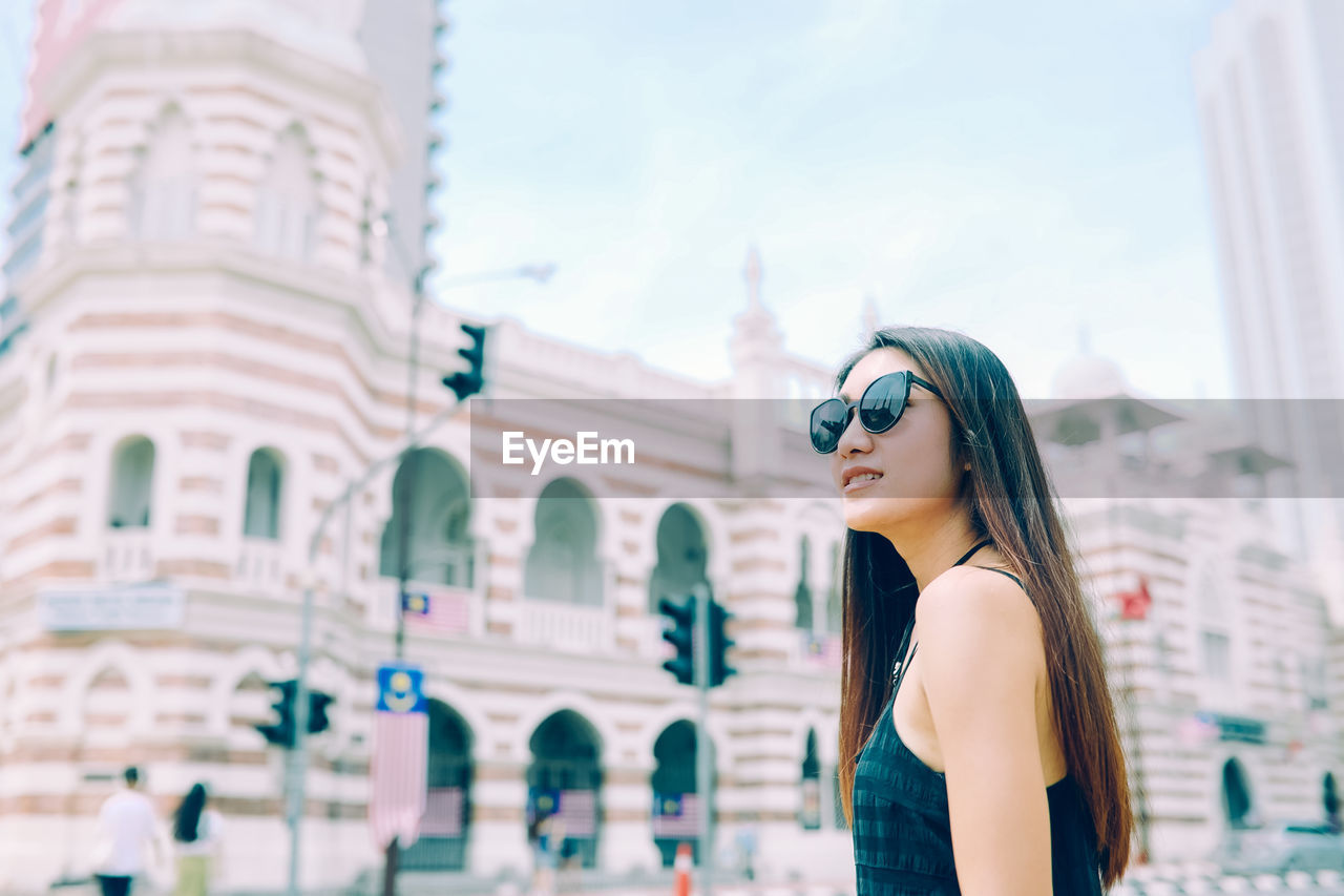 Young woman wearing sunglasses standing against historic building