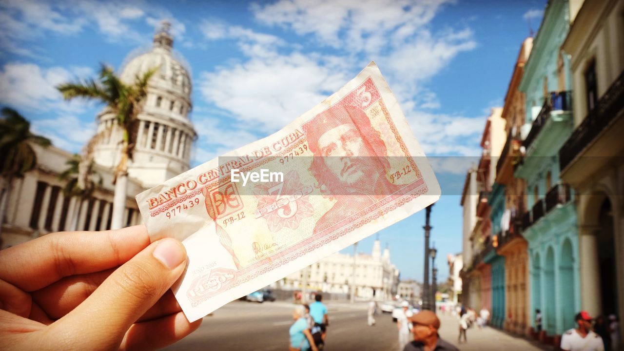 Cropped hand holding paper currency on road in city