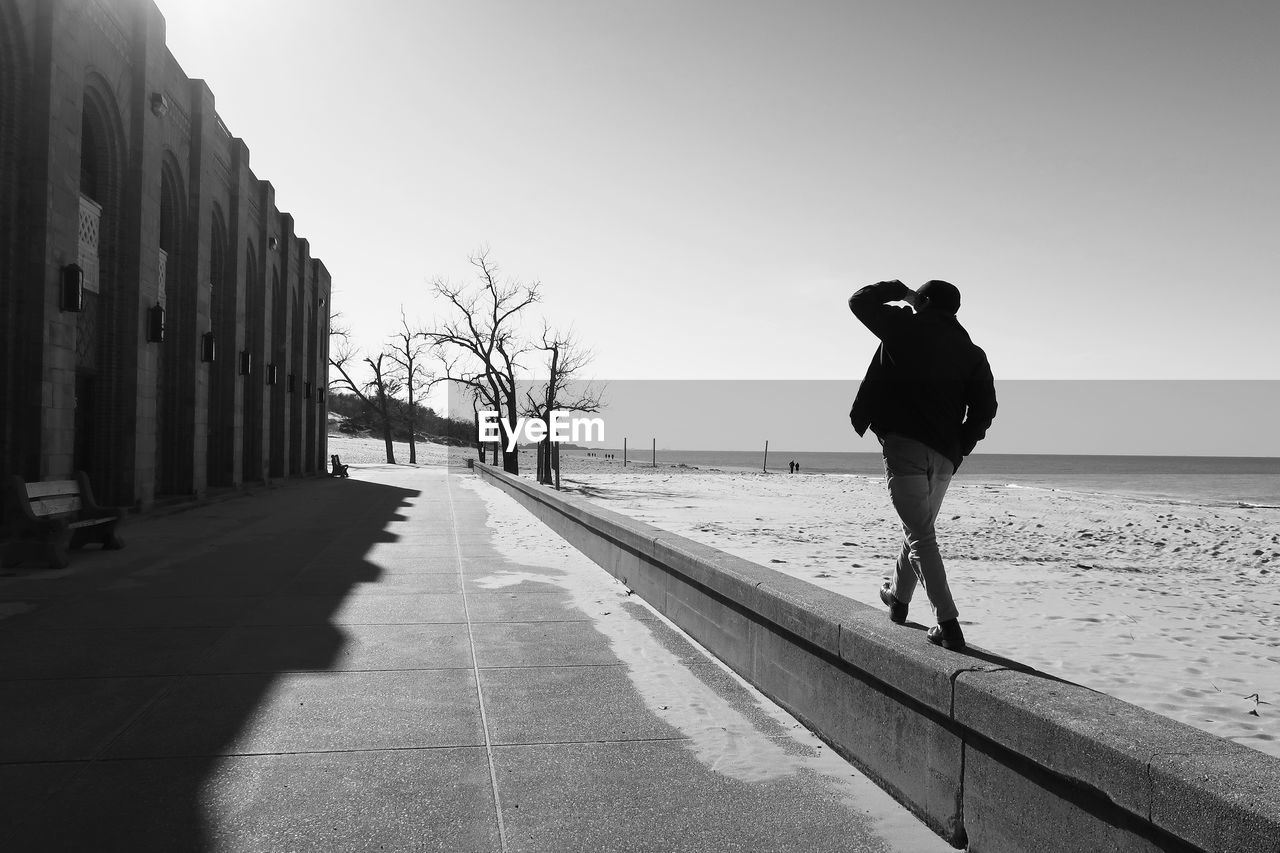Rear view of man walking on retaining wall at beach against sky
