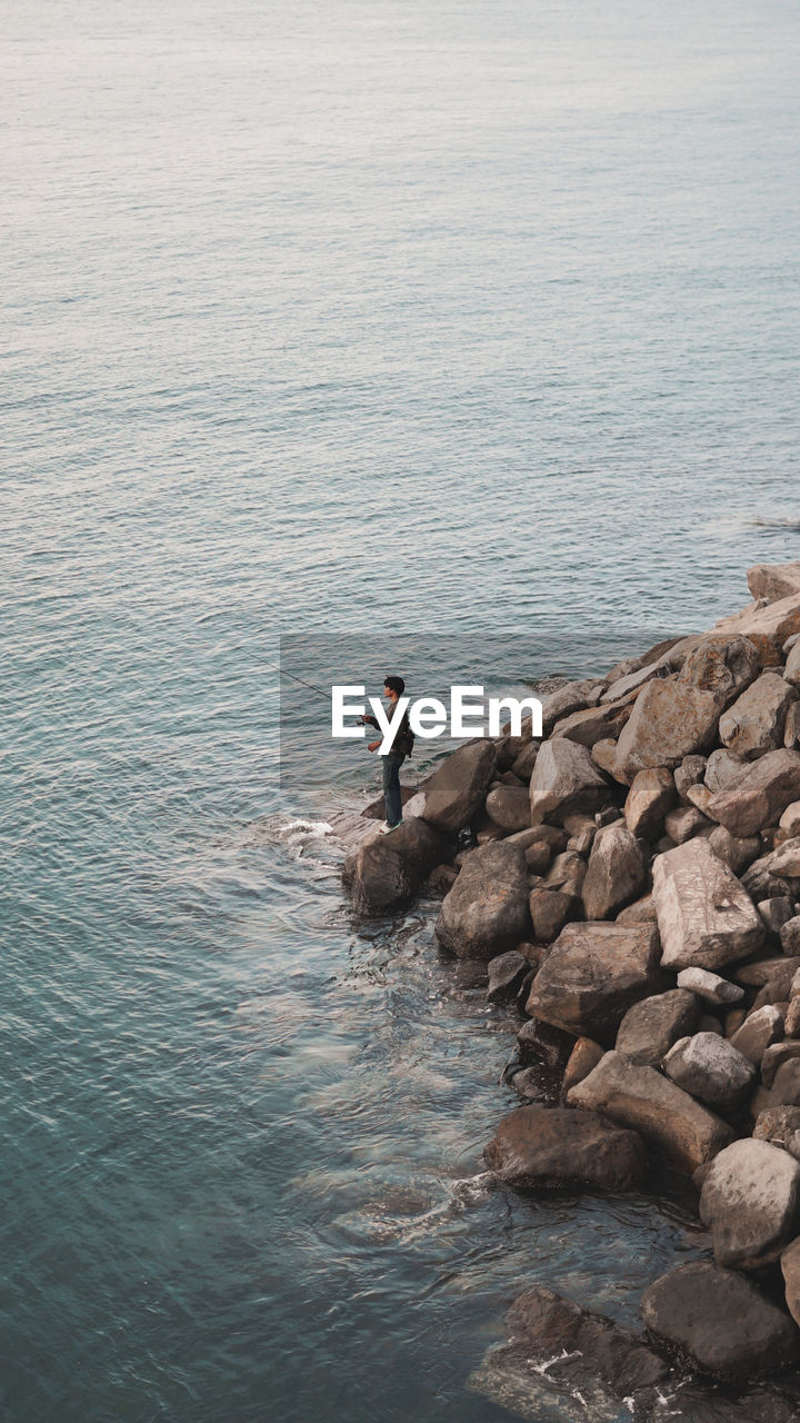 Side view of man on rocks by sea