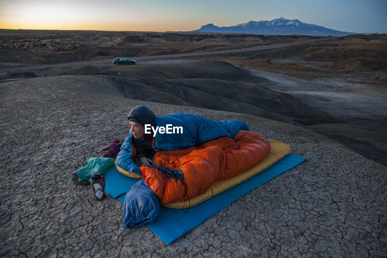 Woman watches sunrise from camp in factory butte badlands, utah