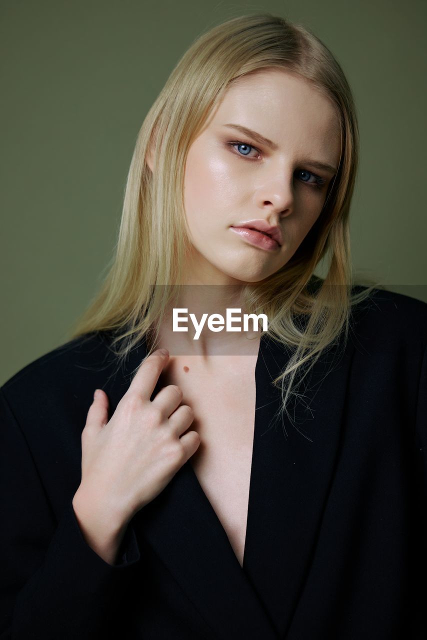 Portrait of young woman wearing blazer against green background