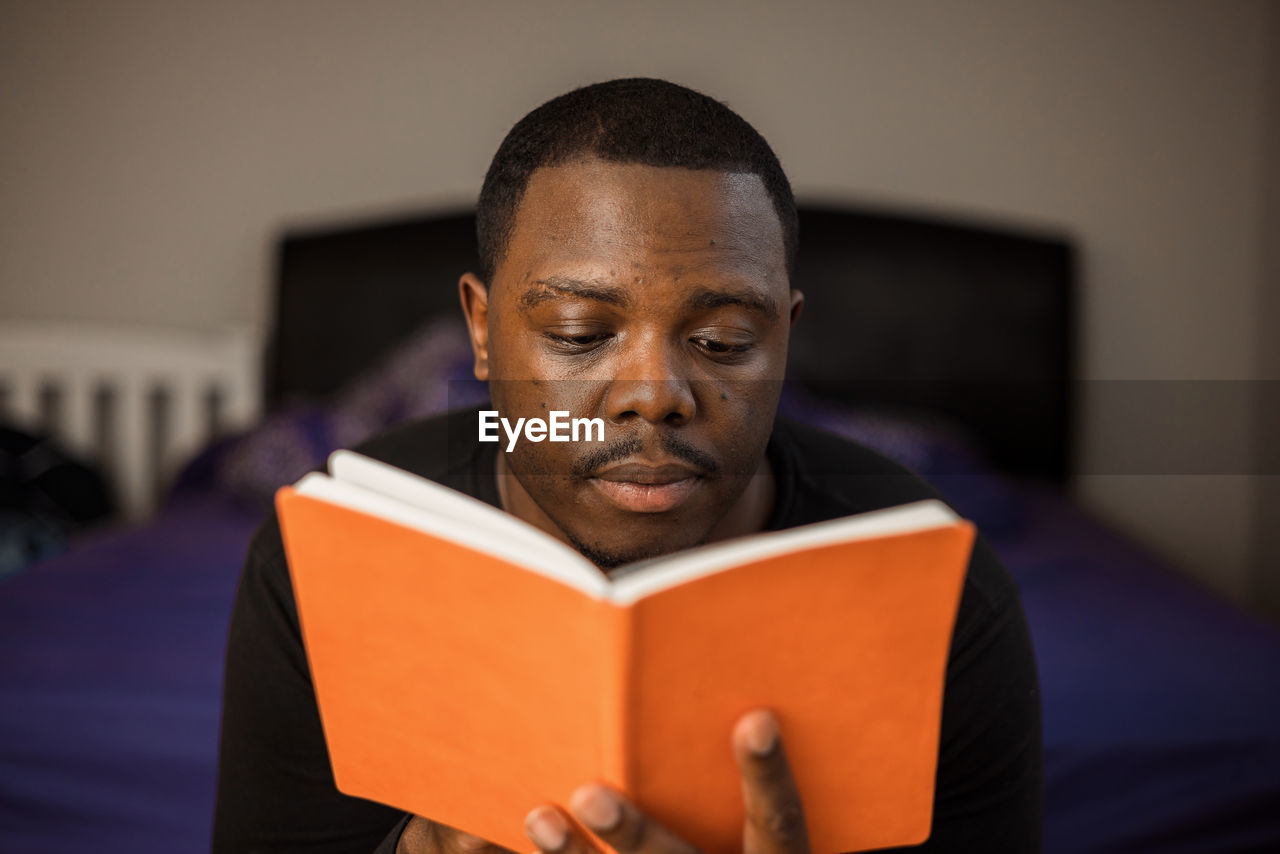 Reading in bed and american american or black man looking at orange literature book