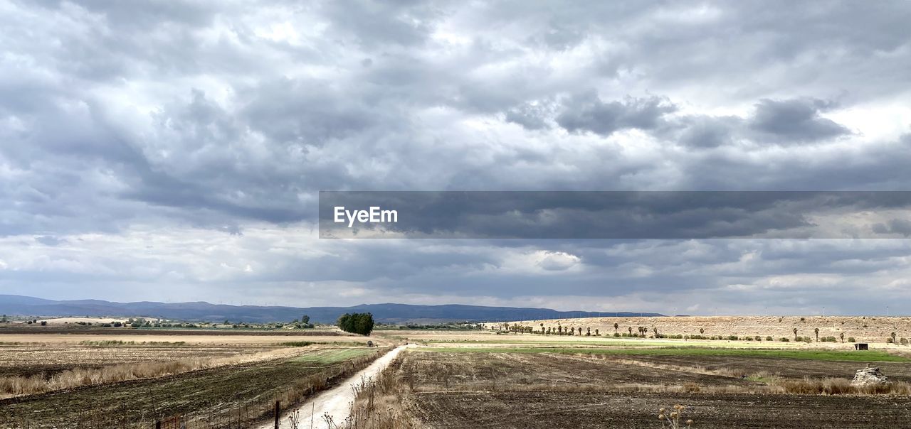 cloud, landscape, environment, sky, field, horizon, nature, land, agriculture, plain, rural scene, rural area, road, scenics - nature, prairie, farm, no people, plant, beauty in nature, cloudscape, hill, soil, transportation, grass, day, travel, horizon over land, dramatic sky, outdoors, overcast, tranquility, non-urban scene, grassland, travel destinations, crop, tranquil scene, storm, dirt, dirt road, cereal plant, steppe, food, storm cloud, tourism, plateau